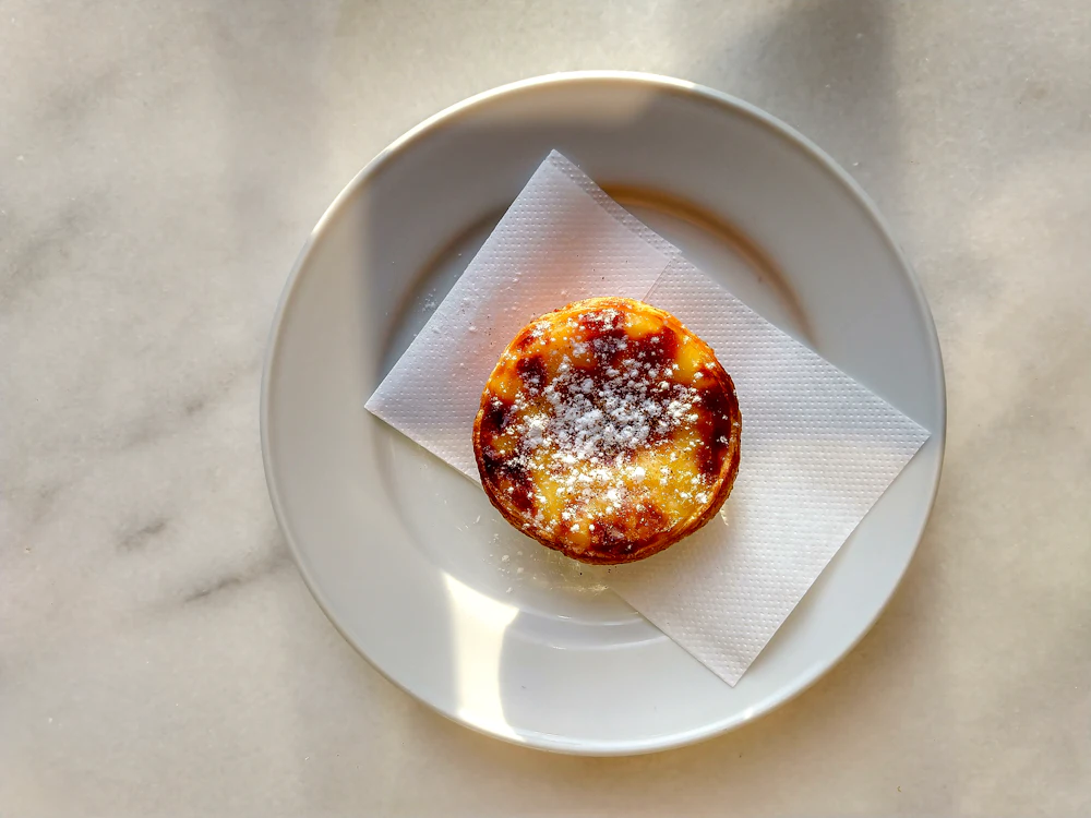 A pastel de nata dusted with sugar on a white plate