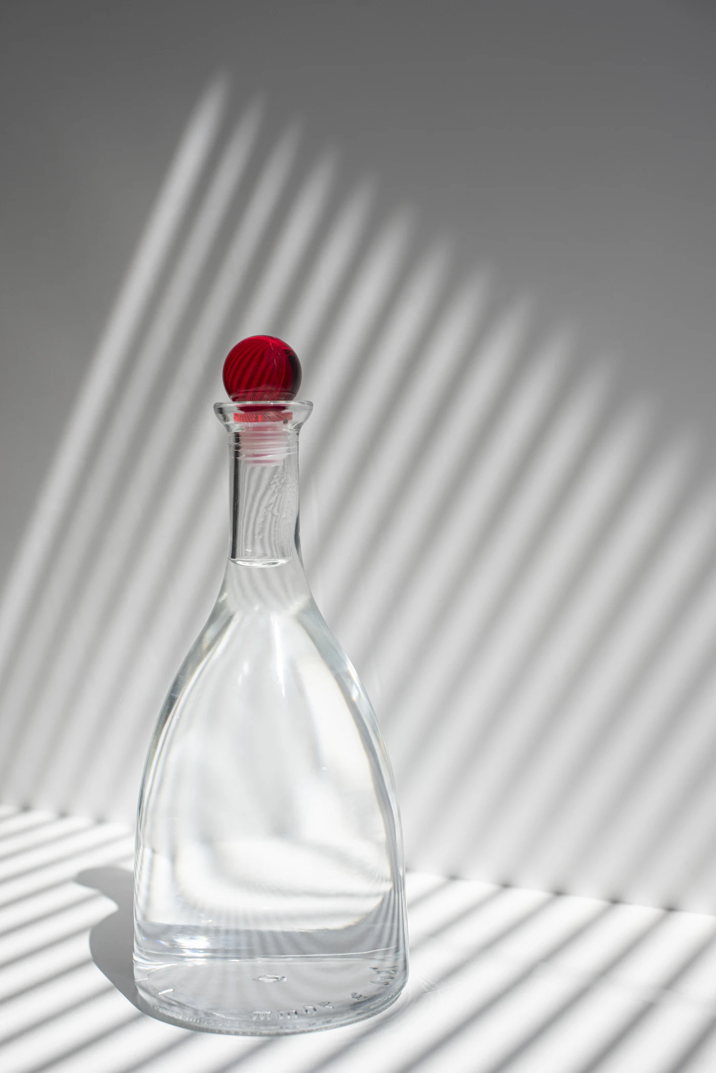 Clear glass carafe with a red stopper in striped shadow